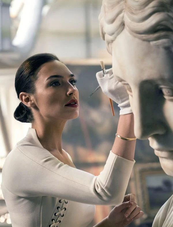 Mujer junto a una escultura clásica de mármol.